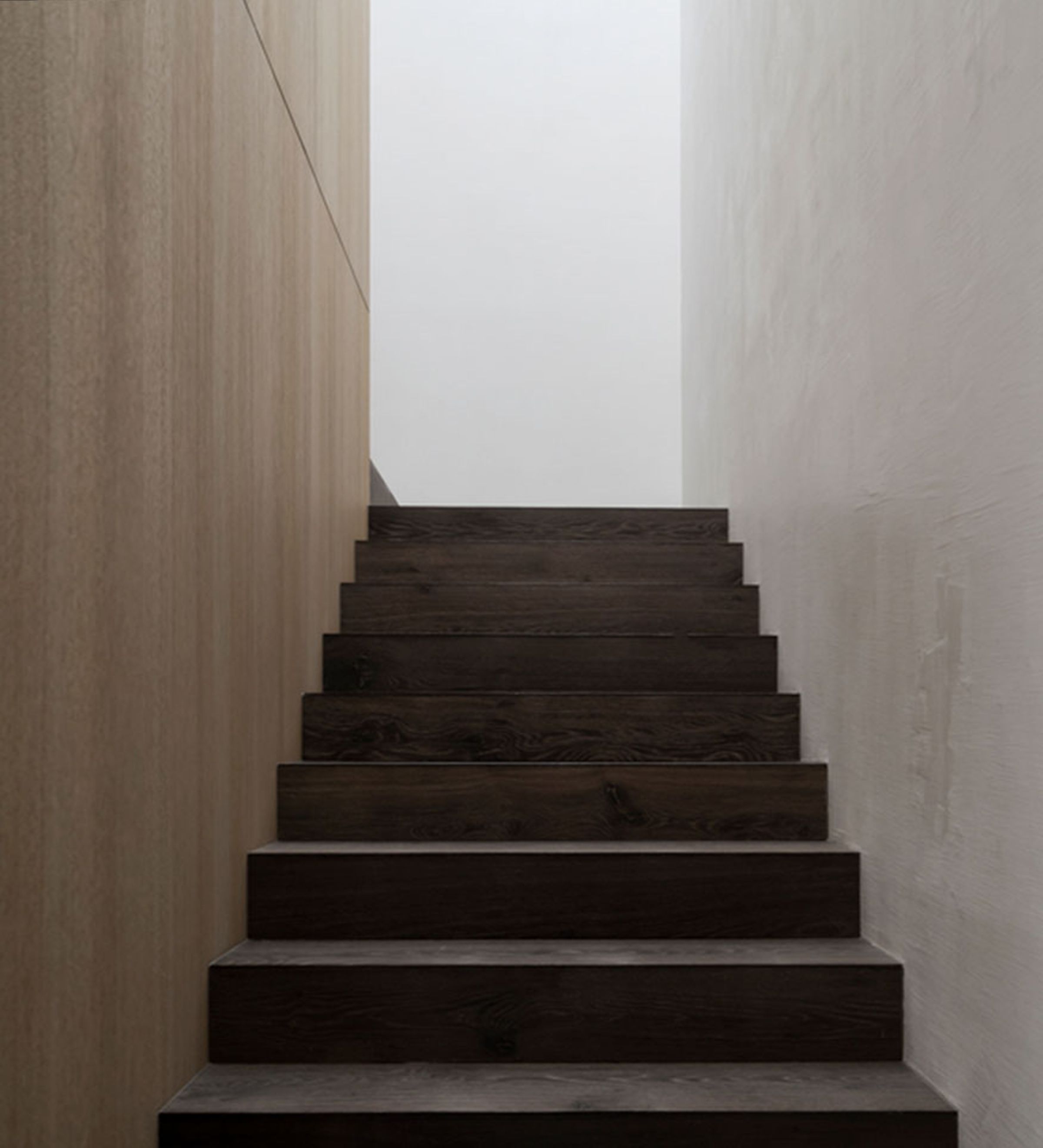 A view from the bottom of a set of dark wood grain stairs which turns 90 degrees left