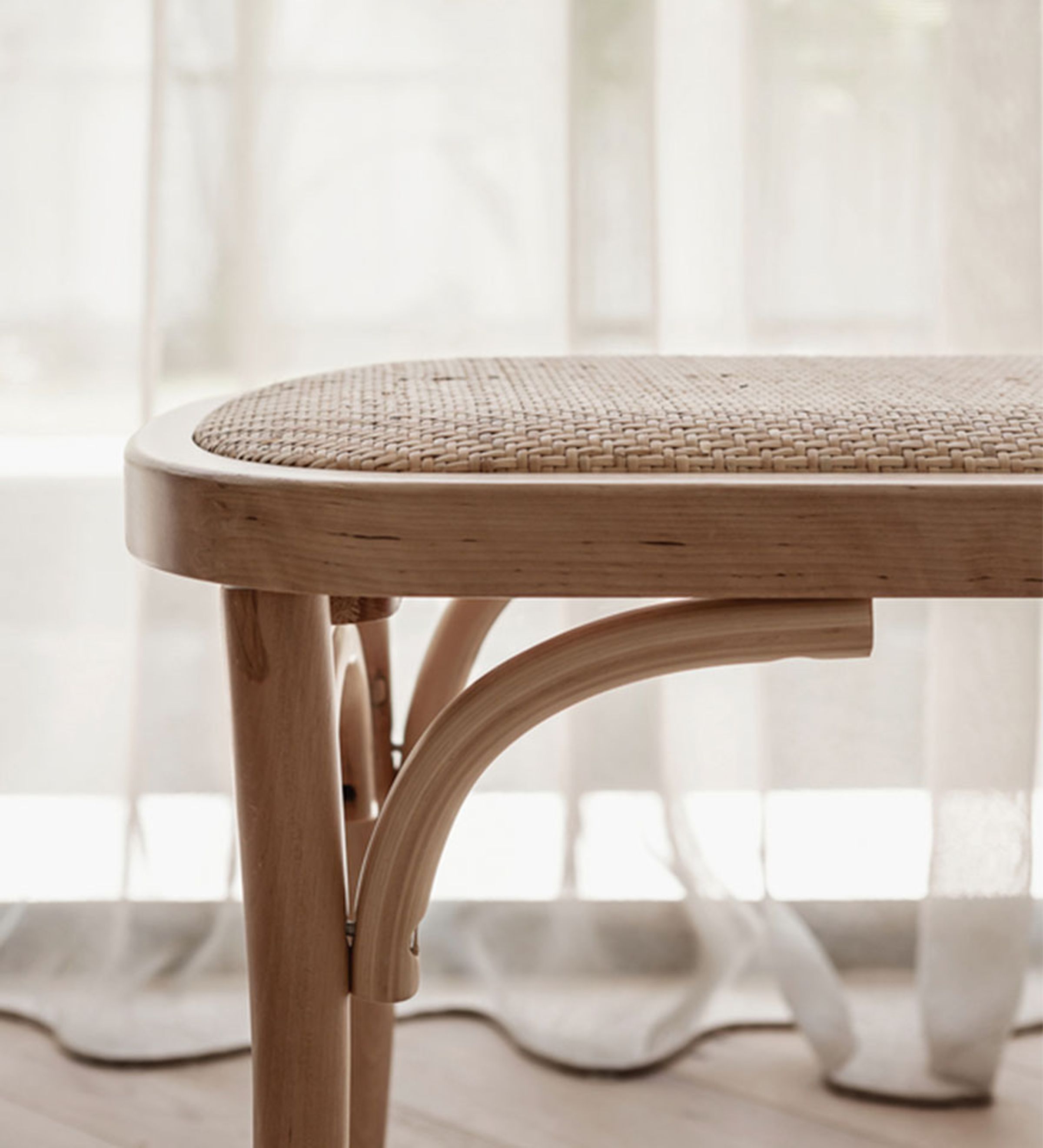 Close up view of a wooden seat with bamboo seat covering in front of a S wave white sheer curtains