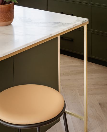 A stool near the corner of a stone bench top, with wood flooring and dark green cabinets behind