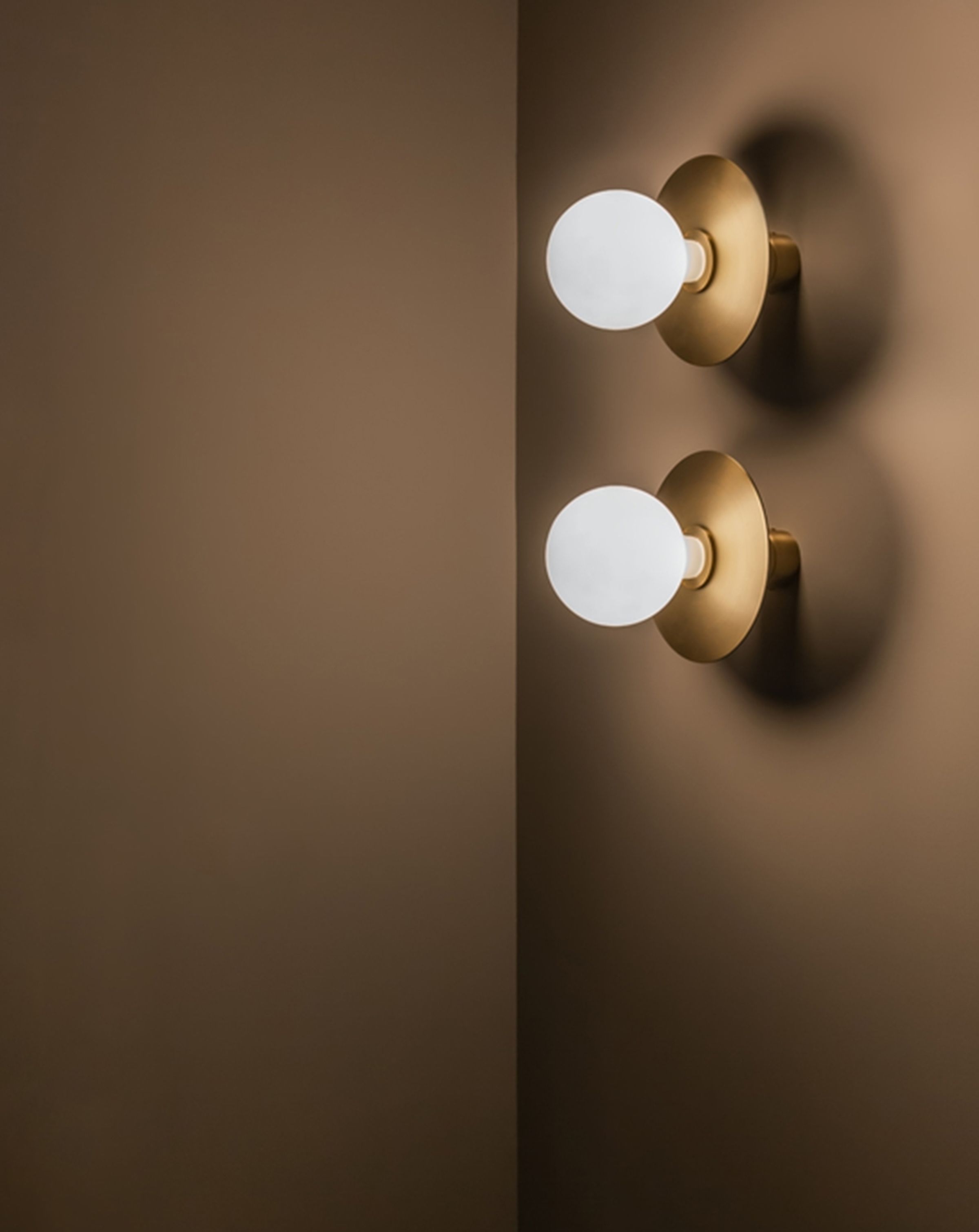 2 circular light bulbs with circular brass fixtures positioned virtually on a right brown wall
