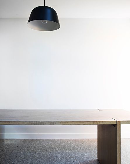 A large rectangular lightly coloured wooden desk with a dark blue down light, with a white wall behind