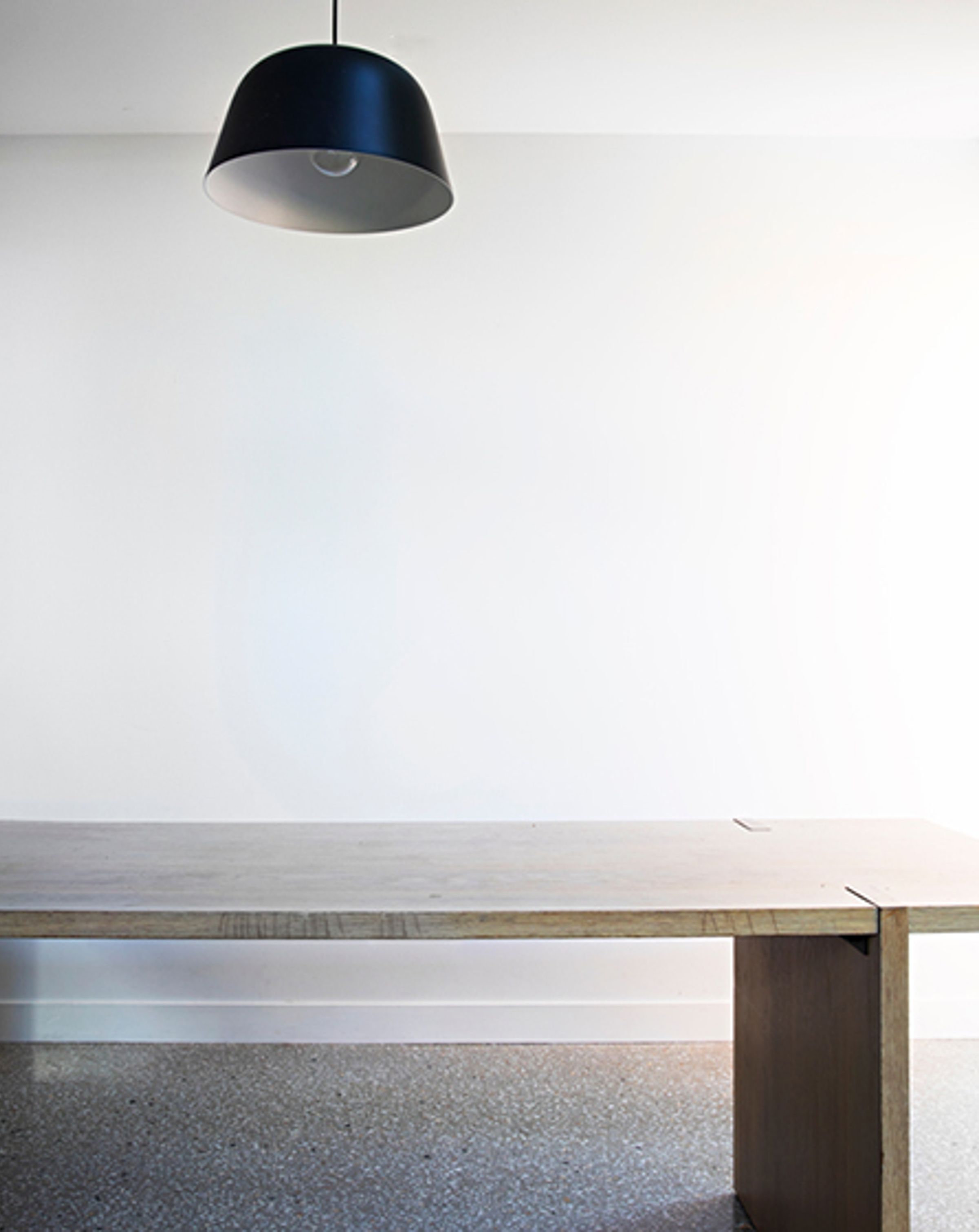 A large rectangular lightly coloured wooden desk with a dark blue down light, with a white wall behind