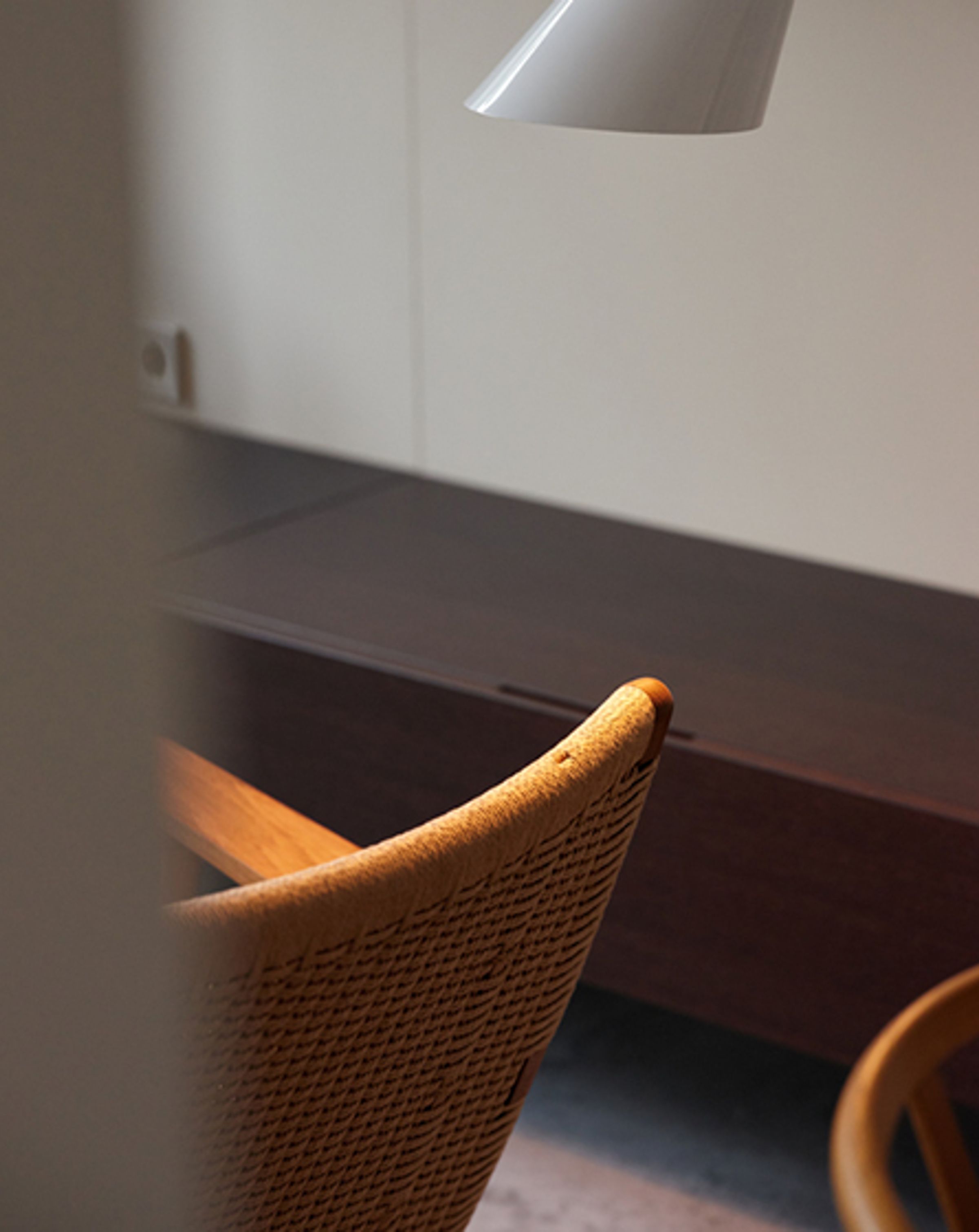 The back of an orange chair in the foreground with low wooden cabinetry in the background and a desk lamp above